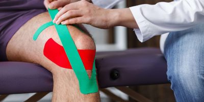 Kinesiology taping.Physical therapist applying kinesiology tape to patient knee.Therapist treating injured knee of young athlete.Post traumatic rehabilitation, sport physical therapy,recovery concept.